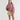 A model wearing a dusty rose oversized crewneck sweatshirt and beige utility shorts with a drawstring waist, photographed against a plain light gray studio background.