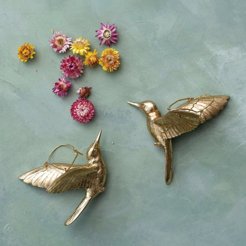 Two gold hummingbird ornaments pictured with flowers. 