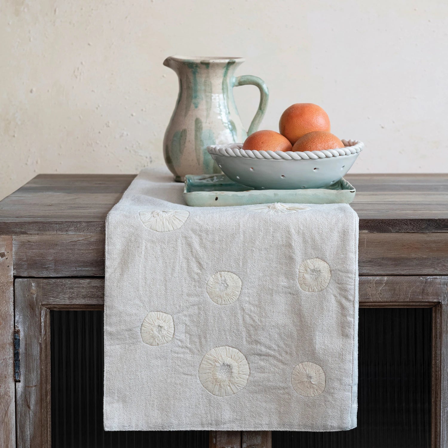 Handmade woven cotton & linen table runner displayed on a wooden table with assorted stoneware. 