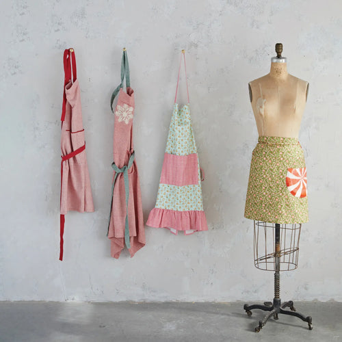 Four different holiday stylish aprons hanging from a wall and styled on a mannequin. 
