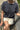 Person wearing a charcoal coloured t-shirt and light-colored shorts sitting outdoors.