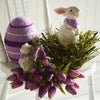 Easter arrangement of an egg, ceramic bunnies and tulips on a white chair. 