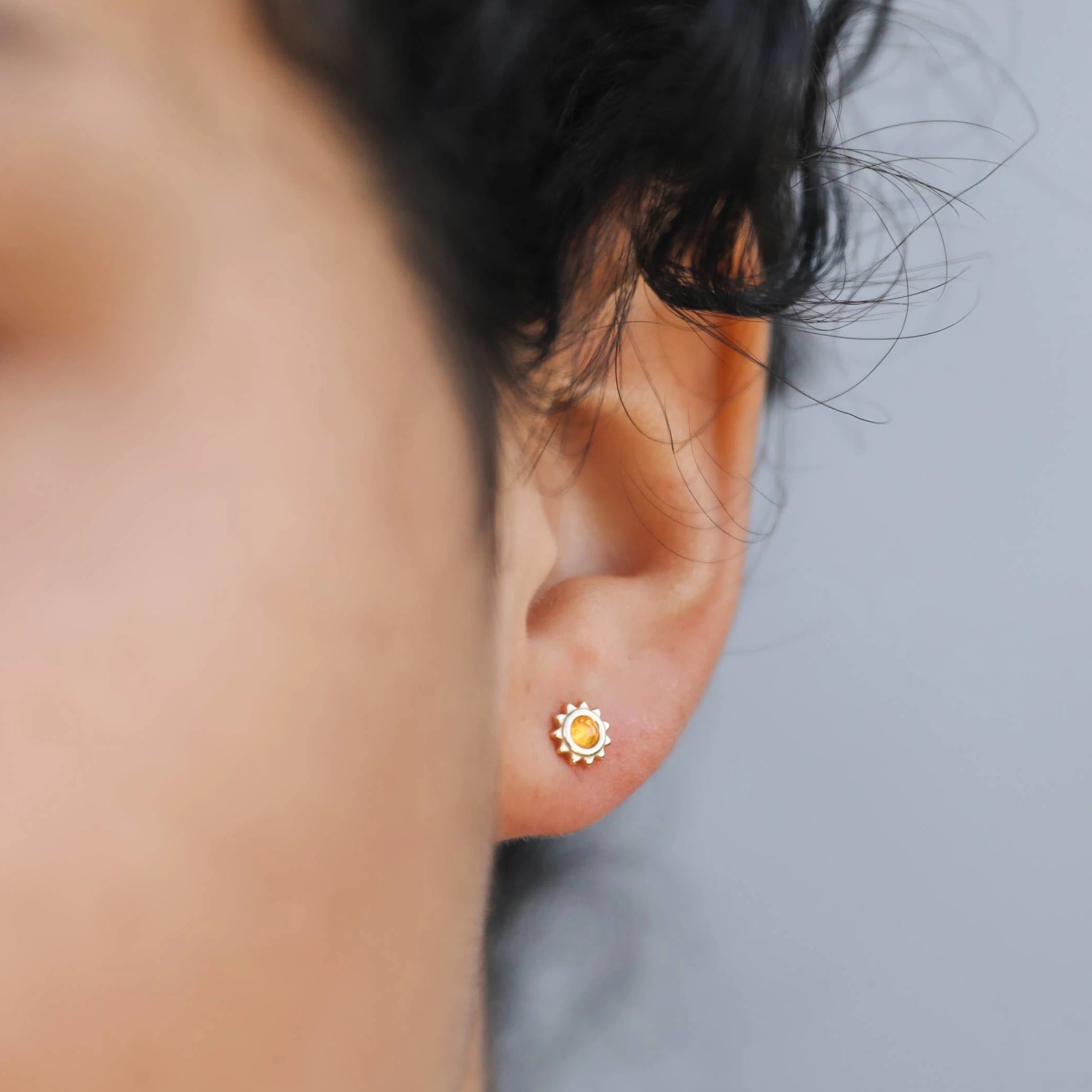 Model wearing Gold plated sun studs with an amber stone in the center. 