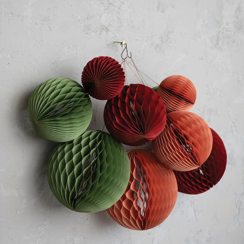 Three different colours of honeycomb paper ornaments hanging from a wall. 