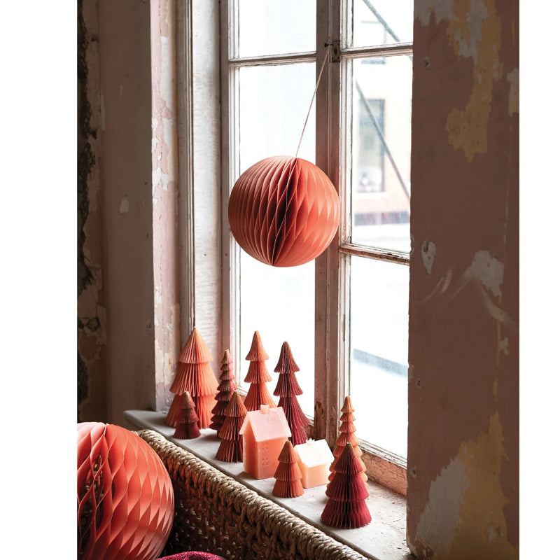 Paper honeycomb ornaments in window with paper trees and house candles in winow sill. 