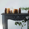 Pinecone candles on a black distressed fireplace mantel with pine boughs in glass vases. 