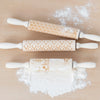 Three carved wooden rolling pins with patterns rolled in some baking flour.