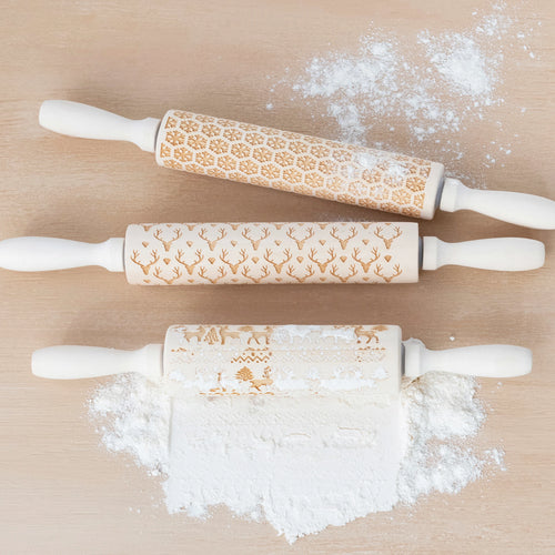 Three carved wooden rolling pins with patterns rolled in some baking flour.