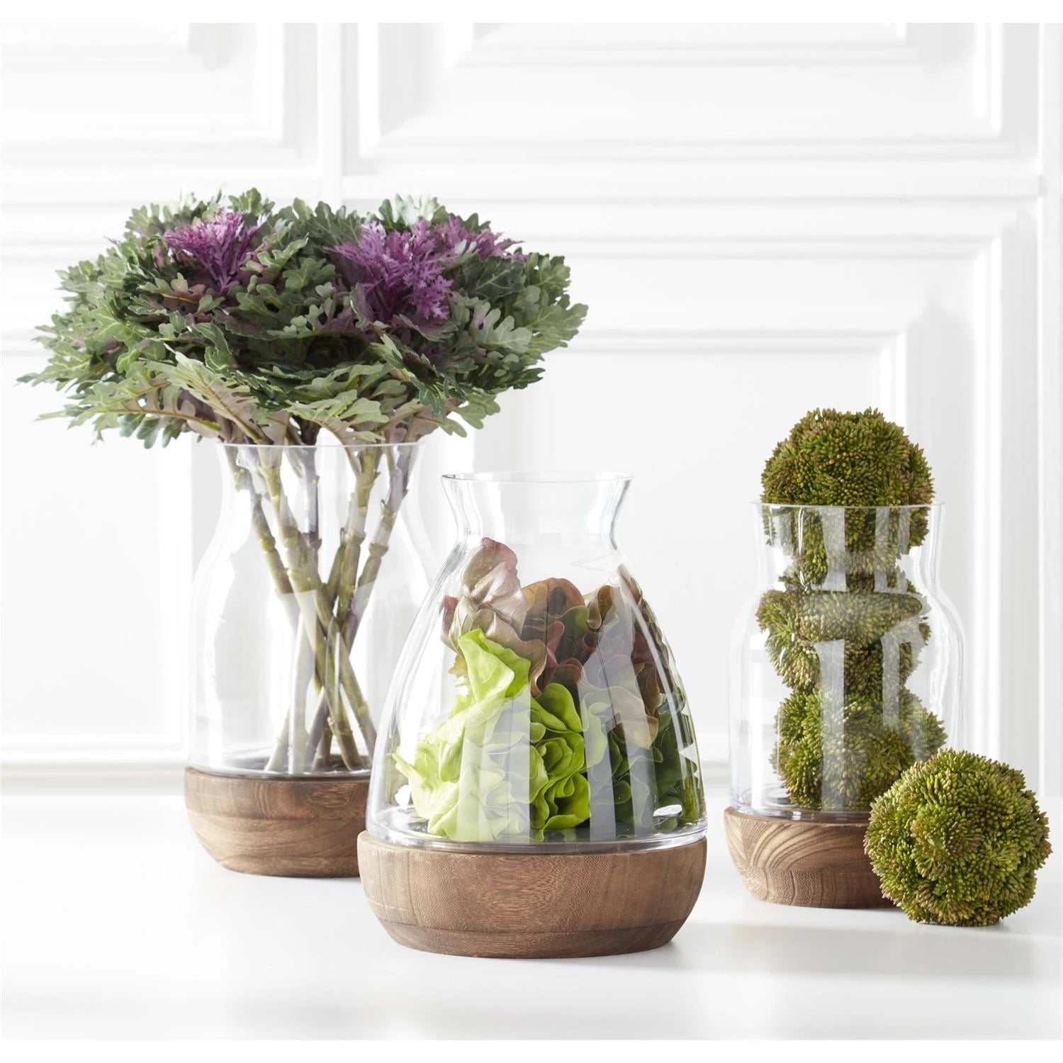 Sedum balls stacked in a clear glass vase on a countertop displayed with fresh flowers. 