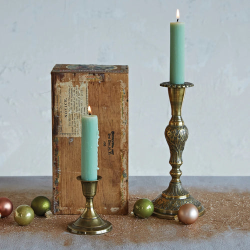 Antique finished brass taper holders with green candles burning. Gold dust and ornaments on the surface.