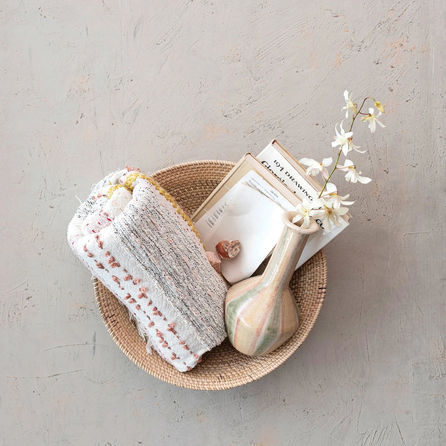Cotton throw basket folded and displayed in a basket with a bud vase and books.