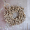 Cream faux berry wreath hung against a chippy paint and textured wall. 