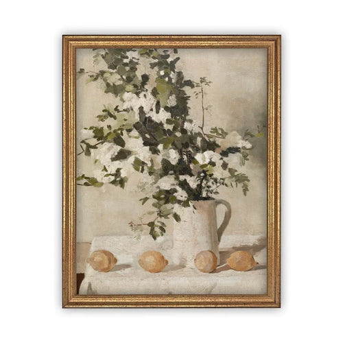 Gold framed vintage inspired artwork with a climbing white rose in a ceramic pitcher. Lemons surround the arrangement on a table. 