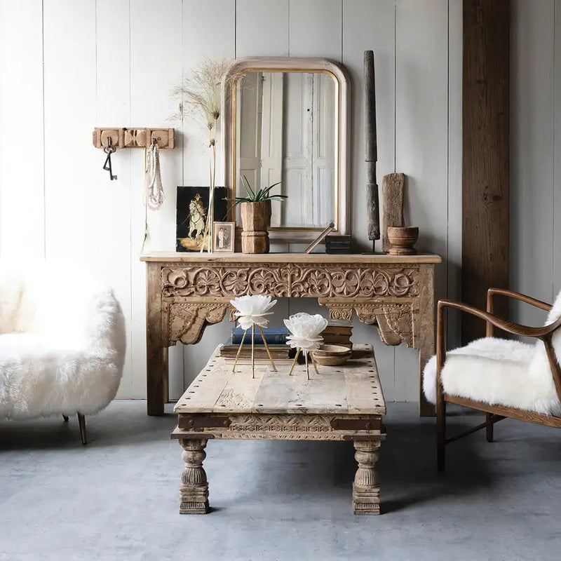Salvaged natural wood console table in living room with white faux fur chairs. 