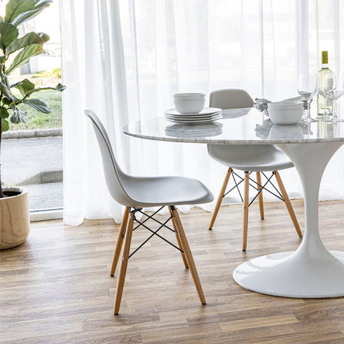 Carrara dining table with white metal tulip base in a dining room with matching chairs and dinnerware. 