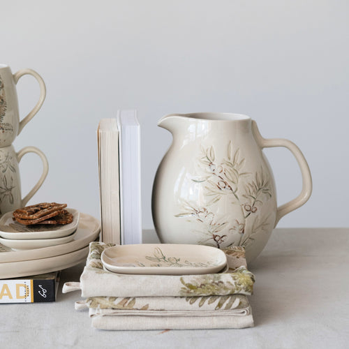Debossed Stoneware Pitcher with Olive Branch styled in kitchen with tea towels and books. 